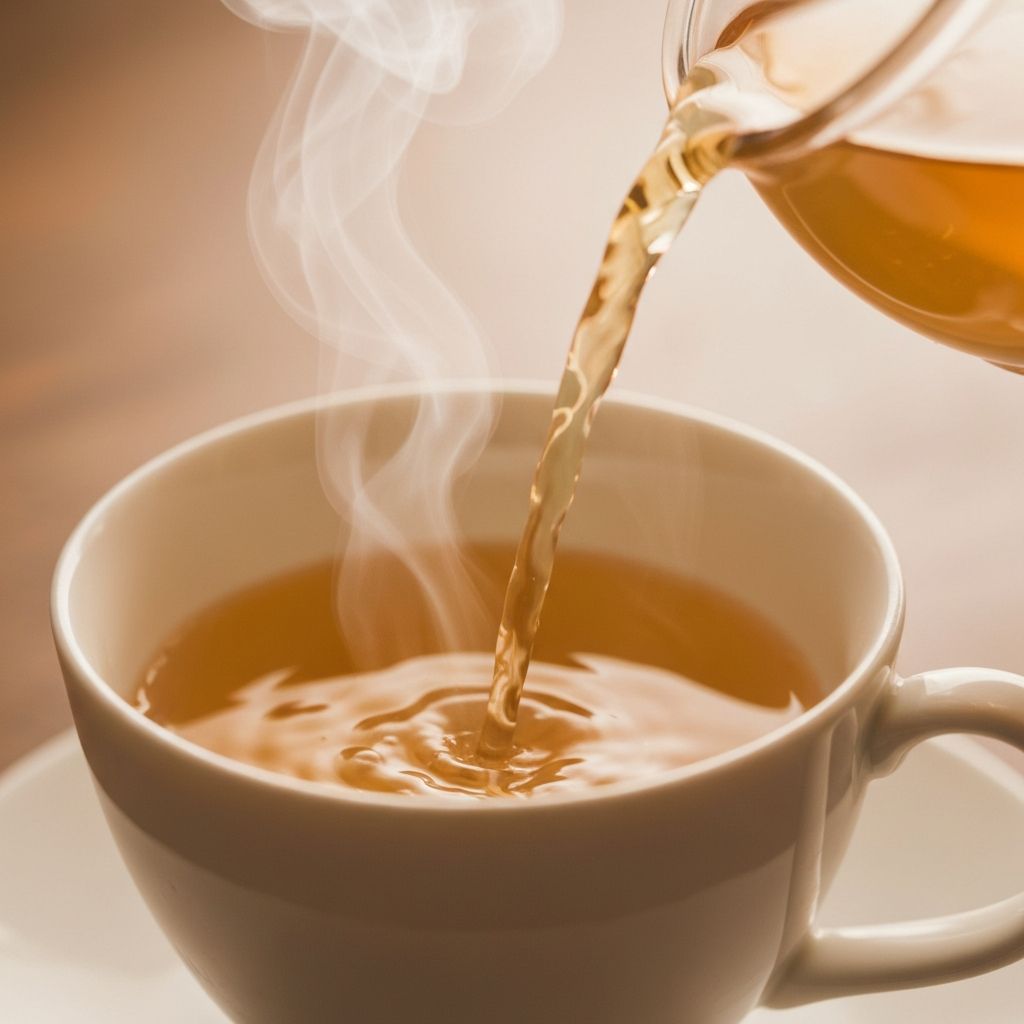 Herbal tea being poured into ceramic cup with steam wisps